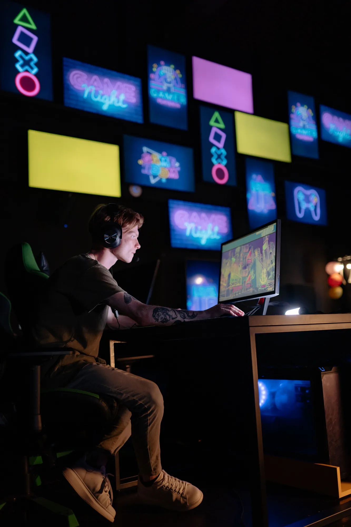 A gamer plays at a computer surrounded by colorful gaming displays.